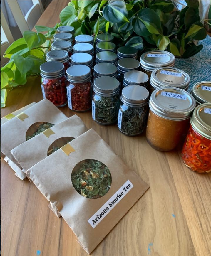 Kraft-paper Arizona Sunrise Tea packets and jars of dried herbs on a wood table.